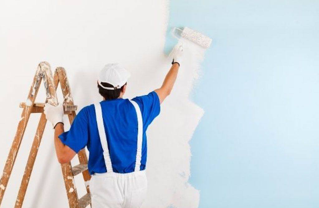 Painter in blue overalls rolling fresh paint onto a wall